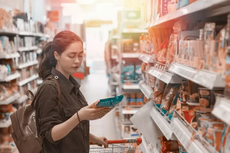 A young pretty woman holds a grocery cart and carefully chooses the products in the store. Light. Close up